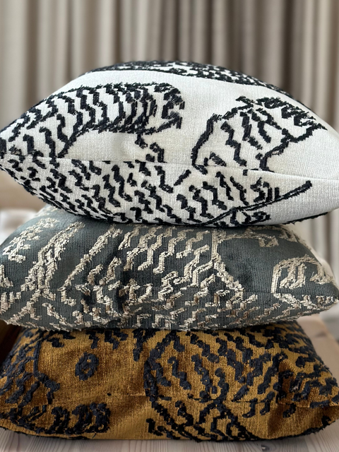 Three Dedar Tiger Mountain cushions stacked on a wooden surface with a neutral background
