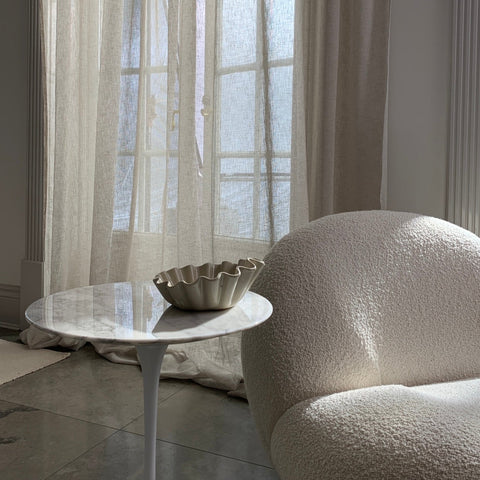 Living room with a textured armchair, marble side table, and sheer bespoke curtains from Moshi Studios